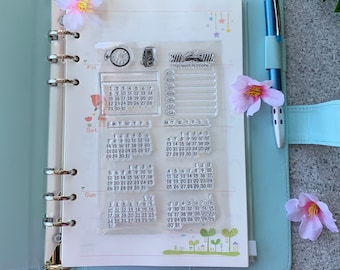May include: A clear plastic sheet with several transparent rubber stamps featuring calendar grids, a clock, a camera, and a line for writing "this week in review".