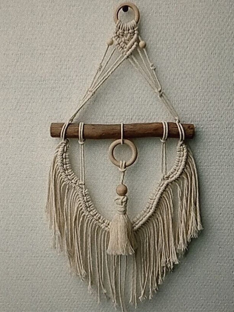 Puede incluir: Un tapiz de macram&eacute; de pared con una barra de madera y un borla. El tapiz est&aacute; hecho con cord&oacute;n de color natural y tiene un dise&ntilde;o geom&eacute;trico.