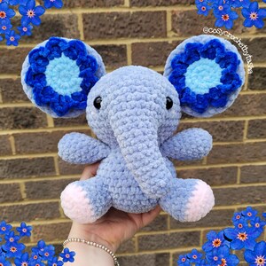 May include: A crocheted plush elephant toy with blue and light blue flower-shaped ears. The elephant is light blue and has a pink nose and feet.