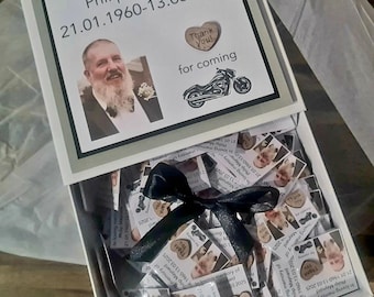 May include: A white box with a black bow, filled with small cards featuring a photo and text. The box lid has text that reads "In loving memory of Philip Maynard 21.01.1960-13.03.2025" with a photo and a motorcycle graphic.