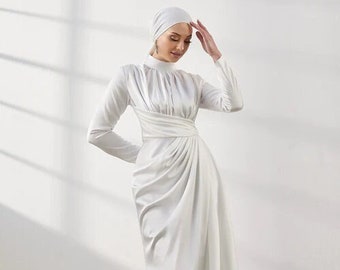 May include: A white satin maxi dress with a high neck and long sleeves. The dress has a draped skirt and a fitted bodice.