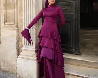 May include: A long, plum-colored dress with a high neckline and tiered skirt. The dress features long sleeves with flared cuffs and is paired with a matching head covering. The outfit is worn outdoors near a stone building.