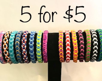 May include: A display of 15 colorful woven bracelets, with a sign that reads "5 for $5". The bracelets are made with different colored rubber bands and are arranged in a row on a black stand.