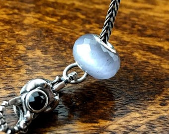 May include: A silver charm bracelet with a gray glass bead and a silver charm with a black stone.