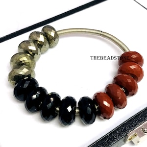 Könnte beinhalten: Armband mit facettierten Perlen in Gold, Schwarz und Rotbraun. Die Perlen sind auf einem silberfarbenen Draht aufgereiht. Der Text "THEBEADSTONE" ist sichtbar. Schmuck.