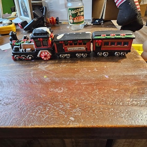 May include: A red, black, and white ceramic train set with a locomotive, a passenger car, and a caboose. The passenger car has the words "Santa's Express" printed on it.