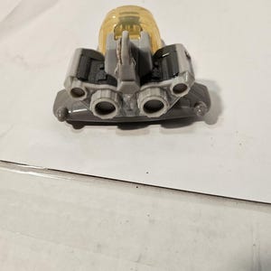 May include: A gray and yellow toy spaceship with multiple exhaust ports and a clear, yellow dome. The toy has a detailed design with various mechanical components, suggesting a futuristic or space-themed toy.