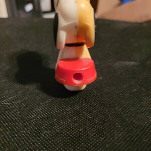 Peut inclure: Un chien en plastique blanc et jaune avec des taches noires. Le chien porte un collier rouge et a un trou au fond de sa base.