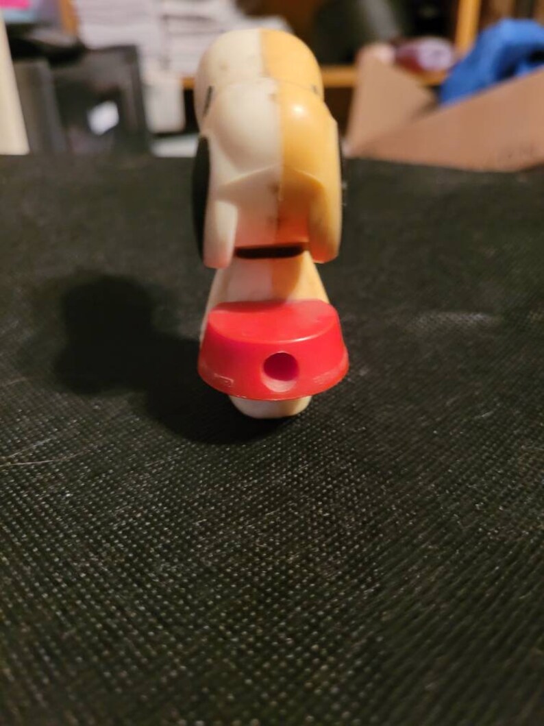 Peut inclure: Un chien en plastique blanc et jaune avec des taches noires. Le chien porte un collier rouge et a un trou au fond de sa base.