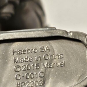 May include: Close-up of a metallic grey object with the text "Hasbro SA Made in China &copy;2015 Marvel C-001C #B2303" embossed on the surface. The object appears to be a part of a larger toy or collectible.