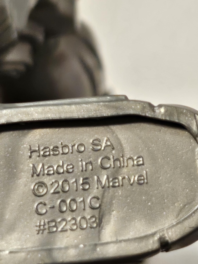 May include: Close-up of a metallic grey object with the text "Hasbro SA Made in China &copy;2015 Marvel C-001C #B2303" embossed on the surface. The object appears to be a part of a larger toy or collectible.