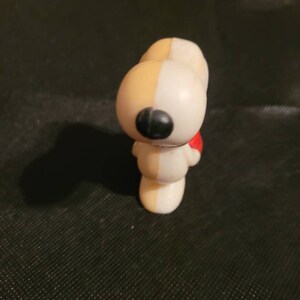 Peut inclure: Une figurine en plastique blanche et jaune de Snoopy, le beagle de la bande dessin&eacute;e Peanuts. Snoopy porte une &eacute;charpe rouge et a un nez noir.