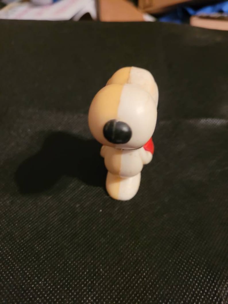 Peut inclure: Une figurine en plastique blanche et jaune de Snoopy, le beagle de la bande dessin&eacute;e Peanuts. Snoopy porte une &eacute;charpe rouge et a un nez noir.