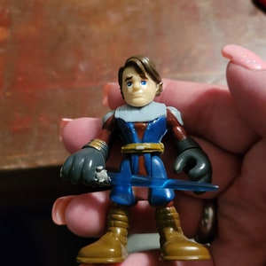 Puede incluir: Una figura de acción azul y marrón de un personaje con una espada láser azul. La figura tiene un cinturón marrón y botas marrones.