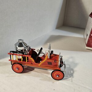 May include: A miniature red fire truck toy with black and yellow accents. The toy has a ladder, a silver tank, and the number 6 on the side. The wheels are red with yellow and black details. A classic toy vehicle.