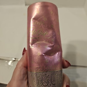 May include: A pink cosmetic tube with gold accents and text. The tube has a decorative band with a paisley design. The text on the tube reads "Avon Treselle" and "Net Wt 3.5 oz".