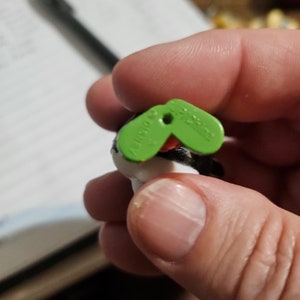 Peut inclure: Gros plan sur une &eacute;tiquette en plastique verte avec le texte "Schleich" dessus. L'&eacute;tiquette est attach&eacute;e &agrave; une petite figurine d'animal en plastique.
