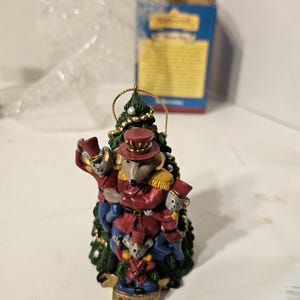 Op de afbeelding: Een kerstversiering uit 2001 met een groep muizen die verkleed zijn als speelgoed soldaten en een groene kerstboom beklimmen. De versiering is gemaakt van geverfd hars en heeft een gouden hanger.