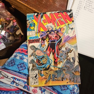 Puede incluir: Una portada de cómic con los X-Men, con Magneto en el centro, vestido con un traje rojo y azul. La portada se titula "Magneto Triumphant" y presenta el logotipo del 30 aniversario. El cómic es de noviembre de 1991.