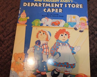 May include: A book cover featuring Raggedy Ann and Raggedy Andy in a department store setting. The title of the book is "Raggedy Ann and Raggedy Andy's Department Store Caper" by Gail George, illustrated by Deborah Borgo.