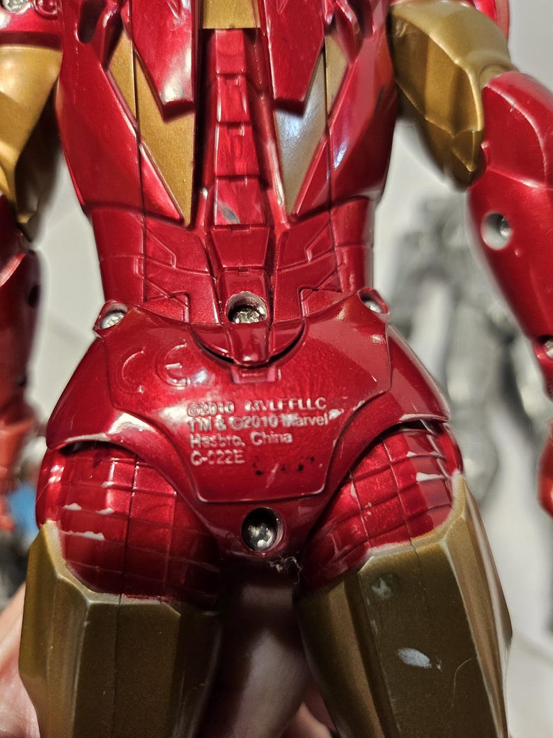 May include: A red and gold Iron Man action figure. The figure has a metallic finish with visible details of the armour. The figure has the text "&copy;2010 MVLFFLLC TM & &copy;2010 Marvel Hasbro, China C-022E" printed on the back.