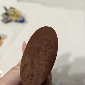 May include: A brown, oval-shaped figurine base with the text "China", "Disney", and "B4" imprinted on it. The figurine base is being held by a person.
