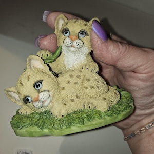 Puede incluir: Figurilla vintage de 1994 de Enesco Younique Cuddle 'n' Cougars de dos cachorros de puma marrones y blancos con hojas verdes sobre una base verde.
