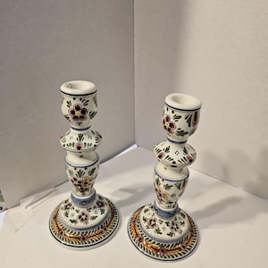 May include: A pair of white ceramic candle holders with a blue, green, yellow, and pink floral design.