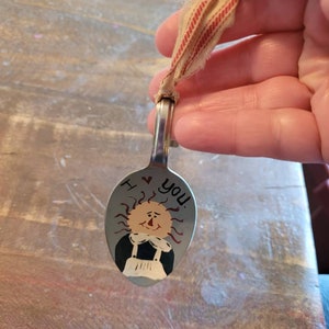 May include: A painted metal spoon with a smiling sun face and the words "I ♥ You".