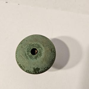 May include: A weathered, round, green object with a central hole. The object has a slightly textured surface and shows signs of wear, with some areas where the green coating is chipped or worn away. The object is likely made of wood or a similar material.