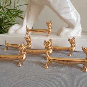 Peut inclure: Un ensemble de cinq repose-baguettes métalliques dorés en forme de chat. Chaque pièce présente un corps long et fin avec une tête de chat à une extrémité, une petite queue à l'autre et un nœud papillon. Les figurines ont une finition lisse.