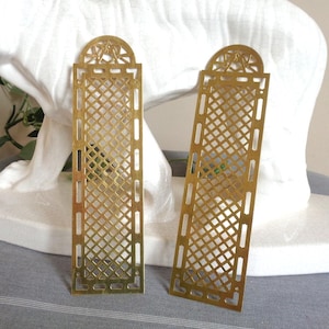 Peut inclure: Deux plaques rectangulaires en laiton avec un motif en treillis et un sommet semi-circulaire orné d'une découpe en étoile. Les plaques métalliques présentent une finition polie et sont orientées verticalement avec un motif ajouré en losange.
