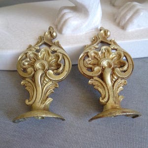 May include: A pair of antique-style, gold-coloured metal furniture accents. Each features a floral design with intricate scrollwork and a curved base. These decorative pieces would add a touch of elegance to any furniture.