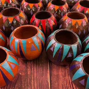 May include: A group of spherical, open-topped containers, hand-painted with geometric designs. The colour palette includes orange, teal, red, and black. The containers are displayed on a wooden surface.
