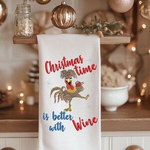 May include: White kitchen towel with red embroidered text that says "Christmas time is better with Wine". A cartoon rooster with a glass of wine is embroidered in the center of the towel.