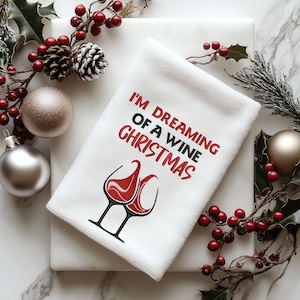 May include: White kitchen towel with red embroidery that reads "I'm Dreaming of a Wine Christmas". Two red wine glasses are embroidered below the text.