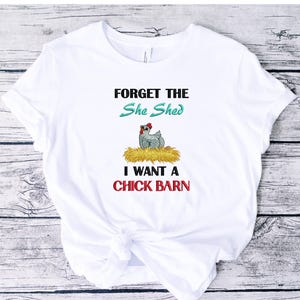 May include: White t-shirt with the text "FORGET THE She Shed I WANT A CHICK BARN". The shirt features a cartoon chicken on a nest of hay. The text is in black, teal, and red.