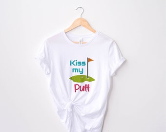 May include: White t-shirt with a green golf course graphic and the text "Kiss my Putt" in colorful letters.