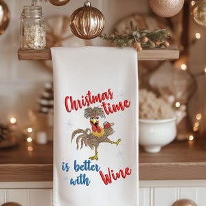 May include: White kitchen towel with an embroidered design of a rooster holding a glass of wine. The text reads "Christmas time is better with wine".