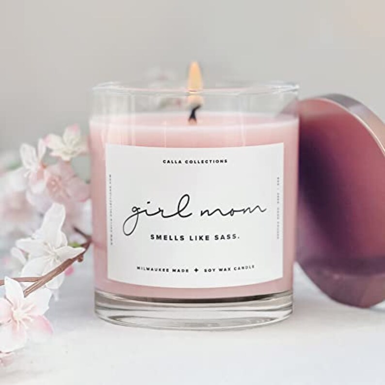 Pu&ograve; includere: Una candela di cera di soia rosa in un barattolo di vetro trasparente con un'etichetta bianca su cui &egrave; scritto "girl mom smells like sass". L'etichetta include anche il testo "Calla Collections, Milwaukee Made, Soy Wax Candle".