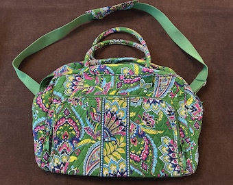May include: Green quilted travel bag with a colorful paisley pattern in shades of pink, blue, and yellow. The bag has a green shoulder strap and handles. A practical and stylish accessory for travel.
