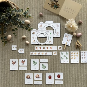 Op de afbeelding: Een set educatieve flashcards voor kinderen met afbeeldingen van dieren, tuingereedschap en nummers. De kaarten zijn gedrukt op wit karton met kleurrijke illustraties. De set bevat een verscheidenheid aan dieren, waaronder kippen, kikkers, slakken en lieveheersbeestjes. Het tuingereedschap omvat een gieter, een hark, een schop en een kruiwagen. De nummers zijn in zwart gedrukt en variëren van 1 tot 14.
