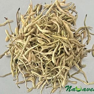 Może przedstawiać: Zbliżenie suszonych kwiatów wiciokrzewu, w jasnobeżowym kolorze. Obraz przedstawia stos suszonych kwiatów, z widocznymi łodygami i pąkami. Logo "Na Aves" jest widoczne w prawym dolnym rogu.