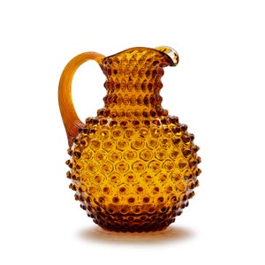 May include: Amber glass pitcher with a textured, bubble-like surface. The pitcher has a round body and a curved handle.