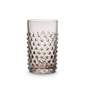 Op de afbeelding: Een transparante glazen tumbler met een getextureerd, geblazen oppervlak. Het glas heeft een grijze tint.