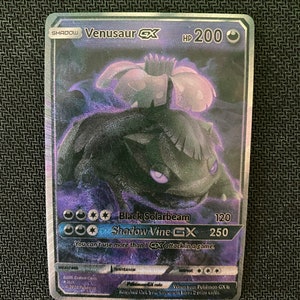 May include: A holographic Pokemon trading card featuring Venusaur GX from the Shadow series. The card is black and purple with a large image of Venusaur in the center. The card's text reads "Shadow Vine GX" and "Black Solarbeam".