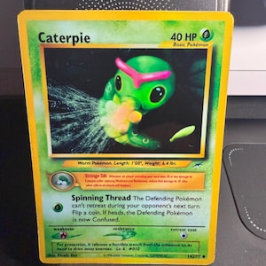 May include: A Pokémon trading card featuring Caterpie, a green worm-like creature with a pink horn. The card has a yellow border and includes text such as "Caterpie", "40 HP", and "Spinning Thread". The card measures 1 foot in length and weighs 6.4 lbs.