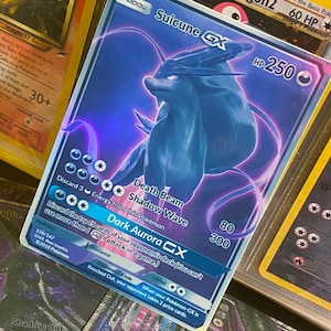 May include: A blue and purple Pokemon card featuring Suicune GX with a holographic effect. The card has a HP of 250 and features the attacks Death Beam, Shadow Wave, and Dark Aurora CX.
