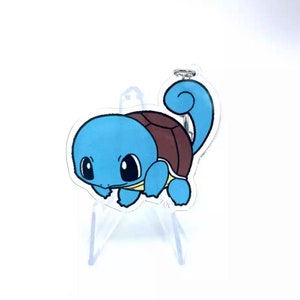 Può includere: Un portachiavi in acrilico trasparente con un personaggio di cartone animato Squirtle blu e marrone. Il portachiavi presenta una piccola illustrazione dettagliata del personaggio Pokémon.
