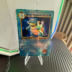 May include: A Blue's Blastoise trading card featuring a blue bipedal turtle character with cannons on its back. The card displays 160 HP, the text Blue's Torrent, and Tidal Blaster. It includes a small illustration of a character in the bottom corner.